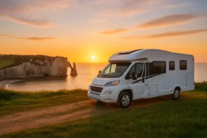 Autocamper parkeret på klippeeng med udsigt til Étretats klippebuer og solnedgang over havet.