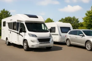 Autocamper og bil med campingvogn parkeret side om side i naturen på en solrig dag.